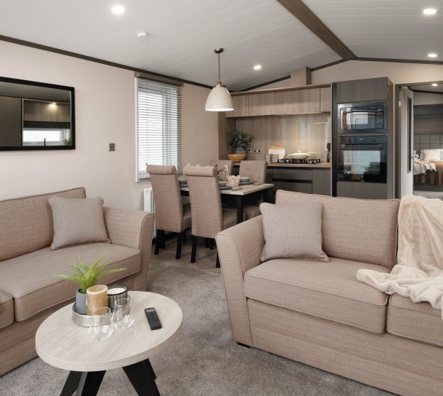 Modern static caravan styled with two light sofas, a cozy dining area, and a well-equipped kitchen.