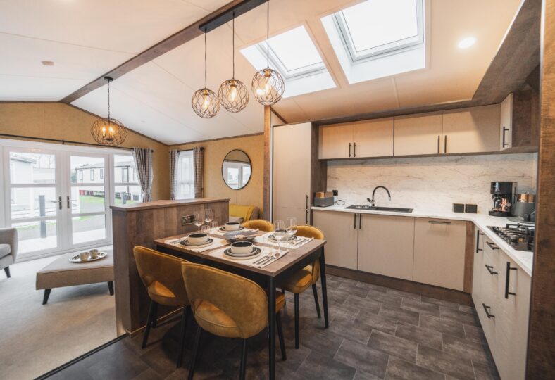 Contemporary static home interior showcasing a modern dining table with elegant hanging lights above, a sleek and sophisticated kitchen, and a stylish living area.