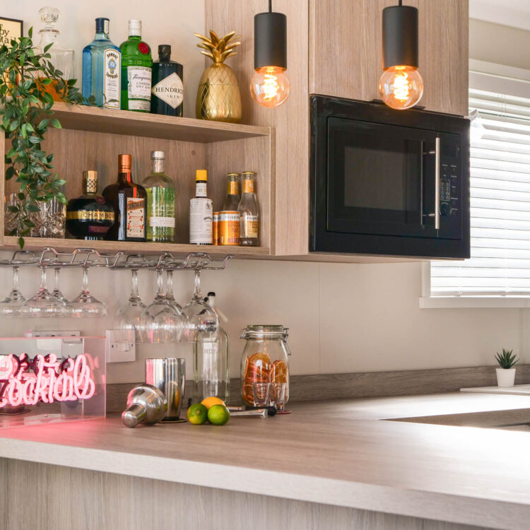 kitchen in faraday lodge - shelves with spirits, built in microwave, sink with brass tap and marble worktop.